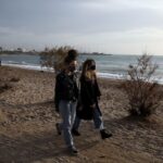 People wearing protective face masks walk on a beach during an unusual warm day, amid the coronavirus disease (COVID-19) pandemic, in the southern suburb of Faliro in Athens