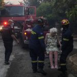 Firefighters-evacuate-an-elderly-woman-from-her-house-in-Penteli-on-Tuesday-July-19-2022.-AP-Photo-Thanassis-Stavrakis